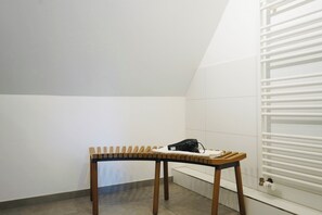 A corner of a room with a white radiator, a wooden bench with a white cushion, and a small white table with a black object on it. - green-man Marktplatz Apartments (Wolfsburg)
