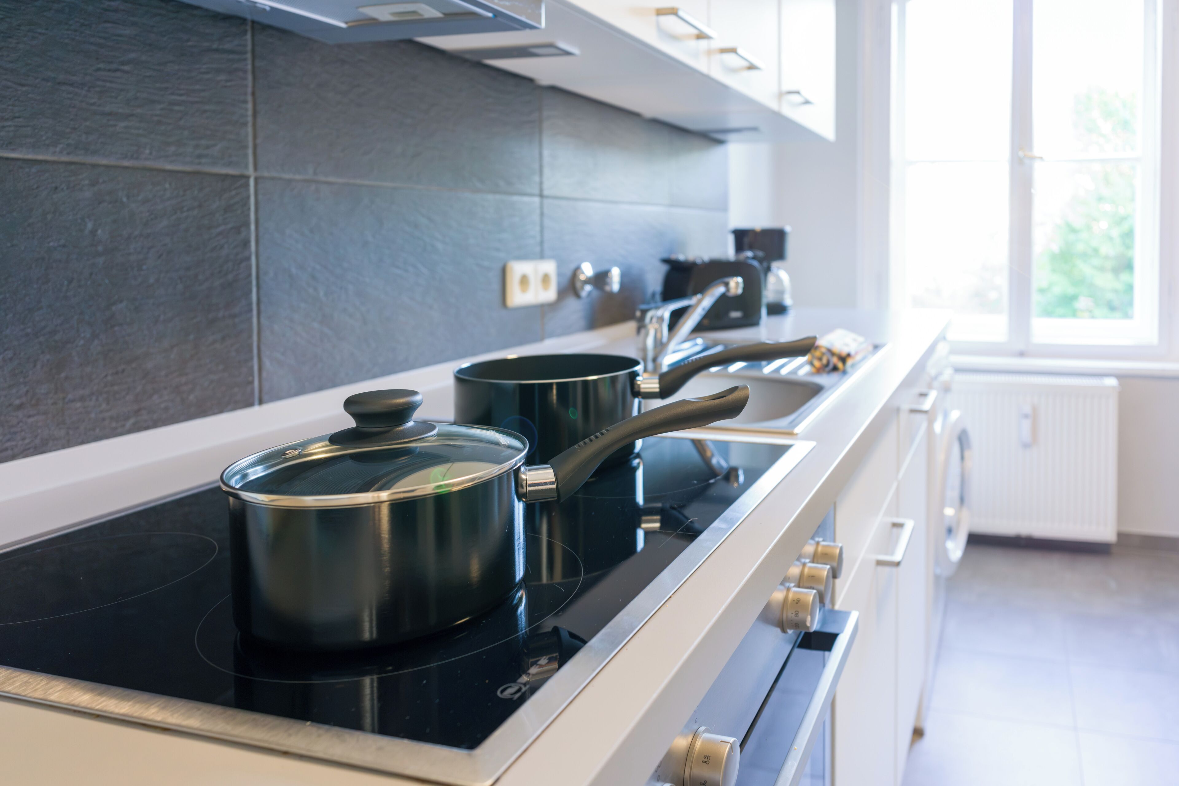 A modern kitchen with a black induction cooktop, stainless steel pots, and a white countertop.