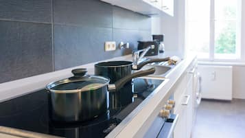 A modern kitchen with a black induction cooktop, stainless steel pots, and a white countertop.