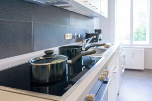 A modern kitchen with a black induction cooktop, stainless steel pots, and a white countertop. - green-man Marktplatz Apartments (Wolfsburg)