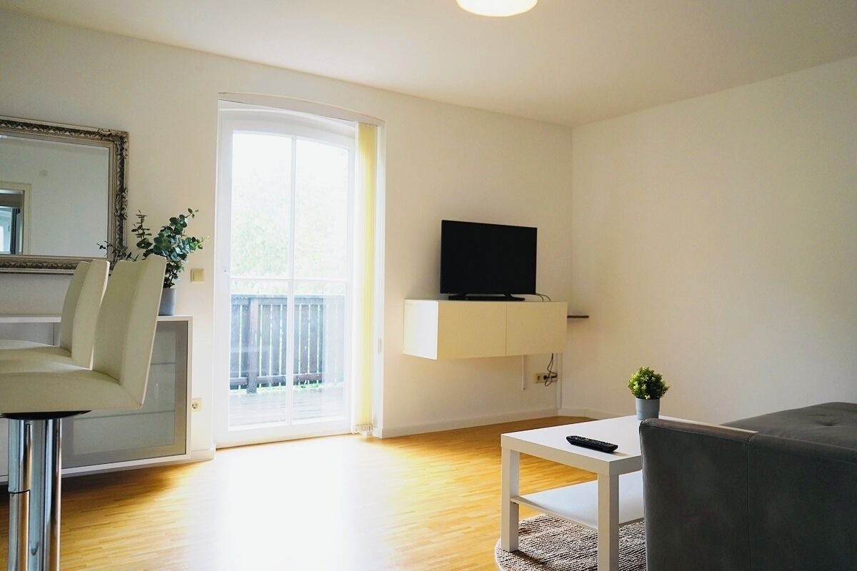 A modern living room with a flat-screen TV, a sofa, a dining area with a chair, and a small table.