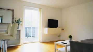 A modern living room with a flat-screen TV, a sofa, a dining area with a chair, and a small table.