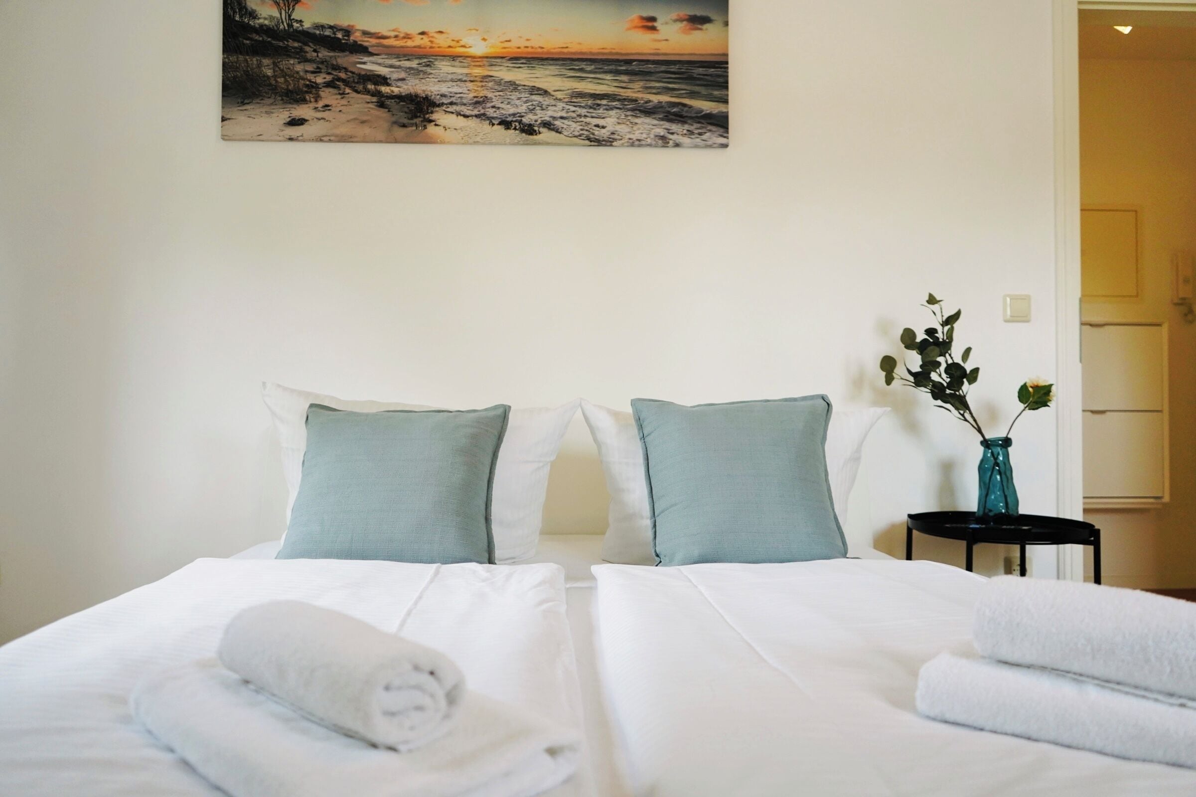 Ein Hotelzimmer mit einem Bett, Kissen, einer Vase mit Blumen und einem Bild an der Wand.