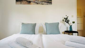 Ein Hotelzimmer mit einem Bett, Kissen, einer Vase mit Blumen und einem Bild an der Wand.