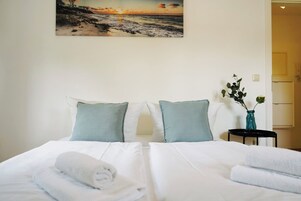 A hotel room with a bed, pillows, a vase with flowers, and a painting on the wall.