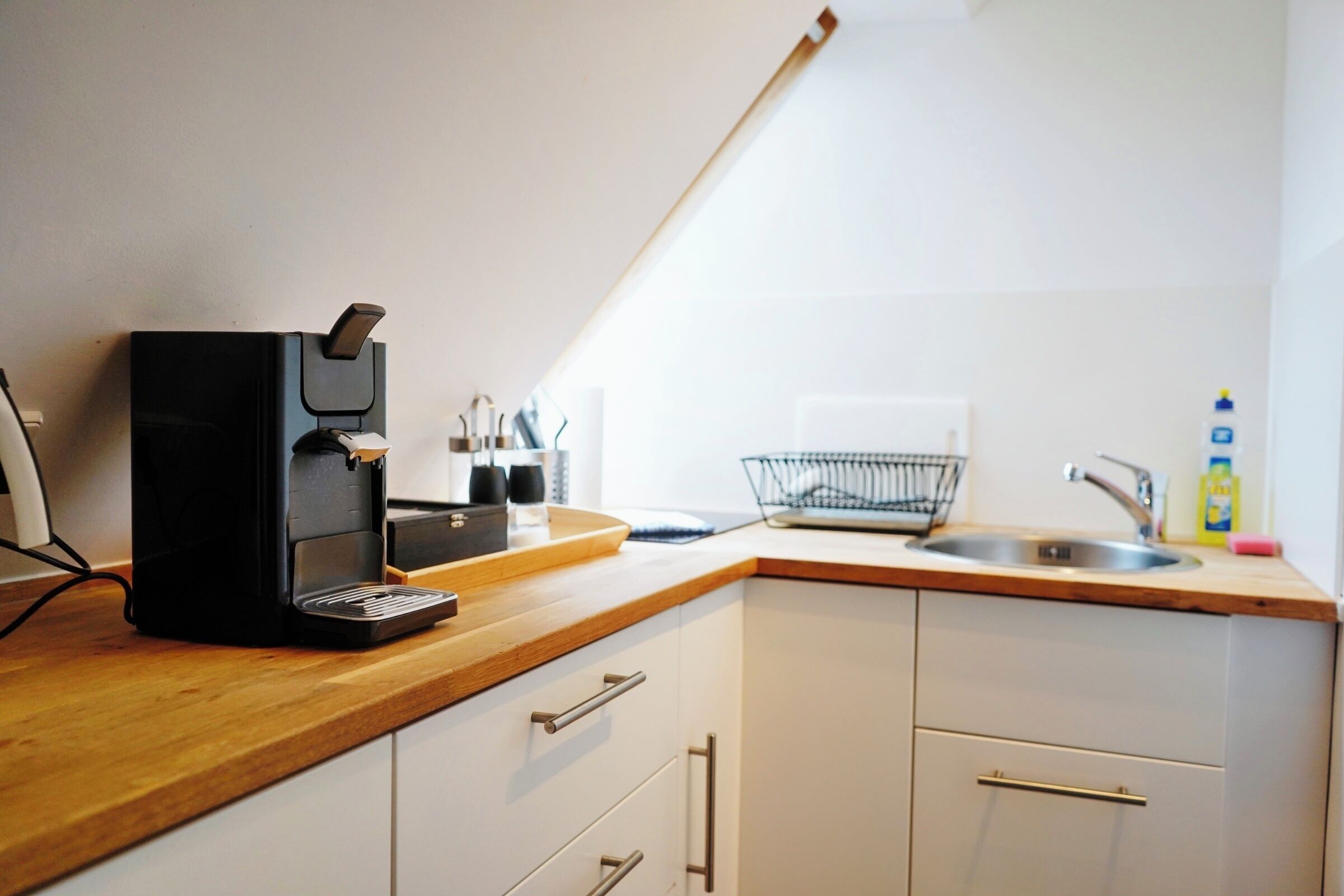 Et køkken med kaffemaskine, vask og bordplade.