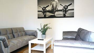 Ein Wohnzimmer mit einem grauen Sofa, einem weißen Couchtisch mit einer Pflanze und einem schwarz-weißen Gemälde von einem Flugzeug an der Wand.