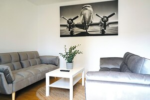 A living room with a grey sofa, a white coffee table with a plant, and a black and white airplane painting on the wall.