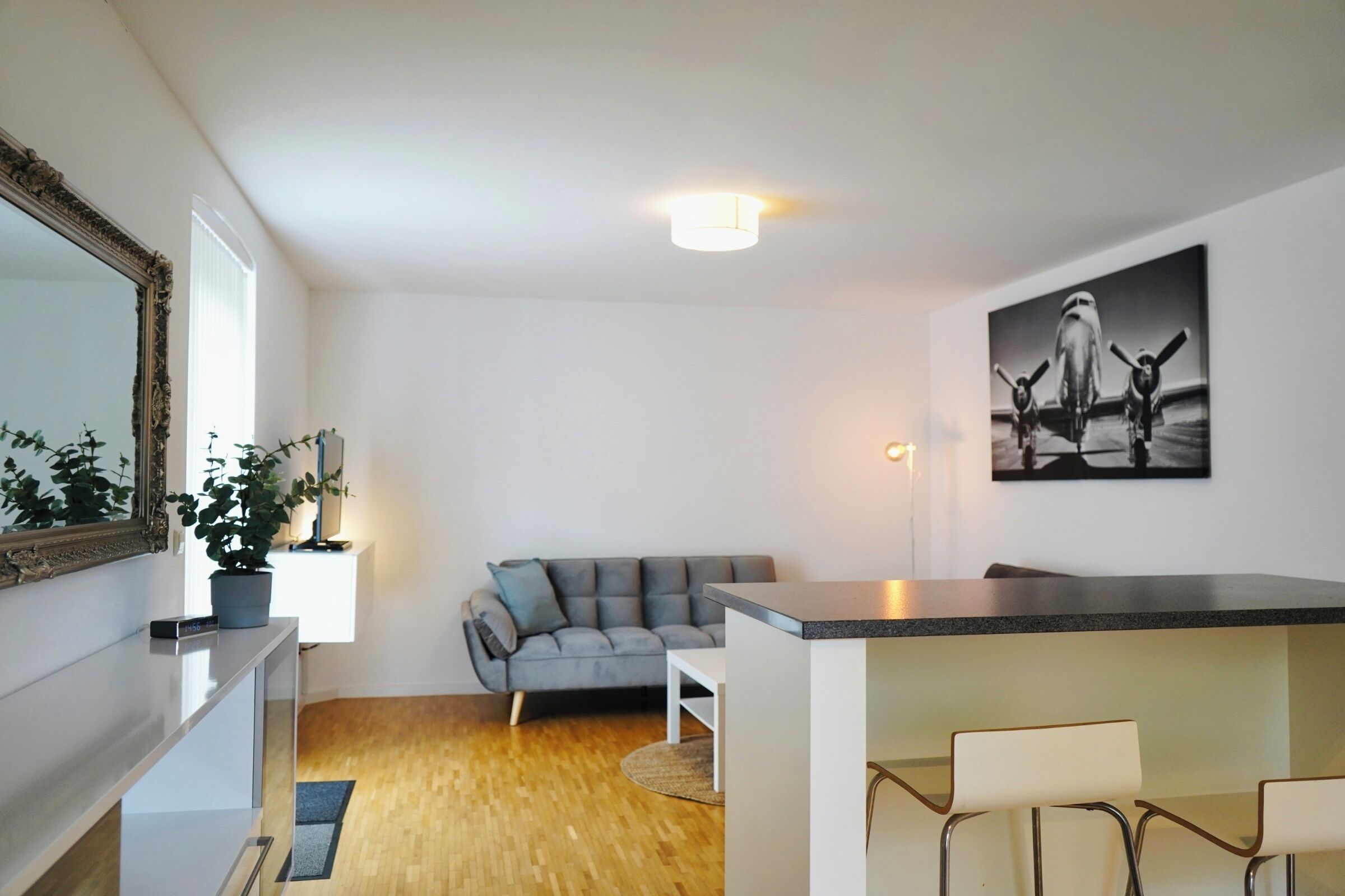 Ein modernes Wohnzimmer mit einem grauen Sofa, einem Essbereich mit Bar und einem großen Spiegel links.