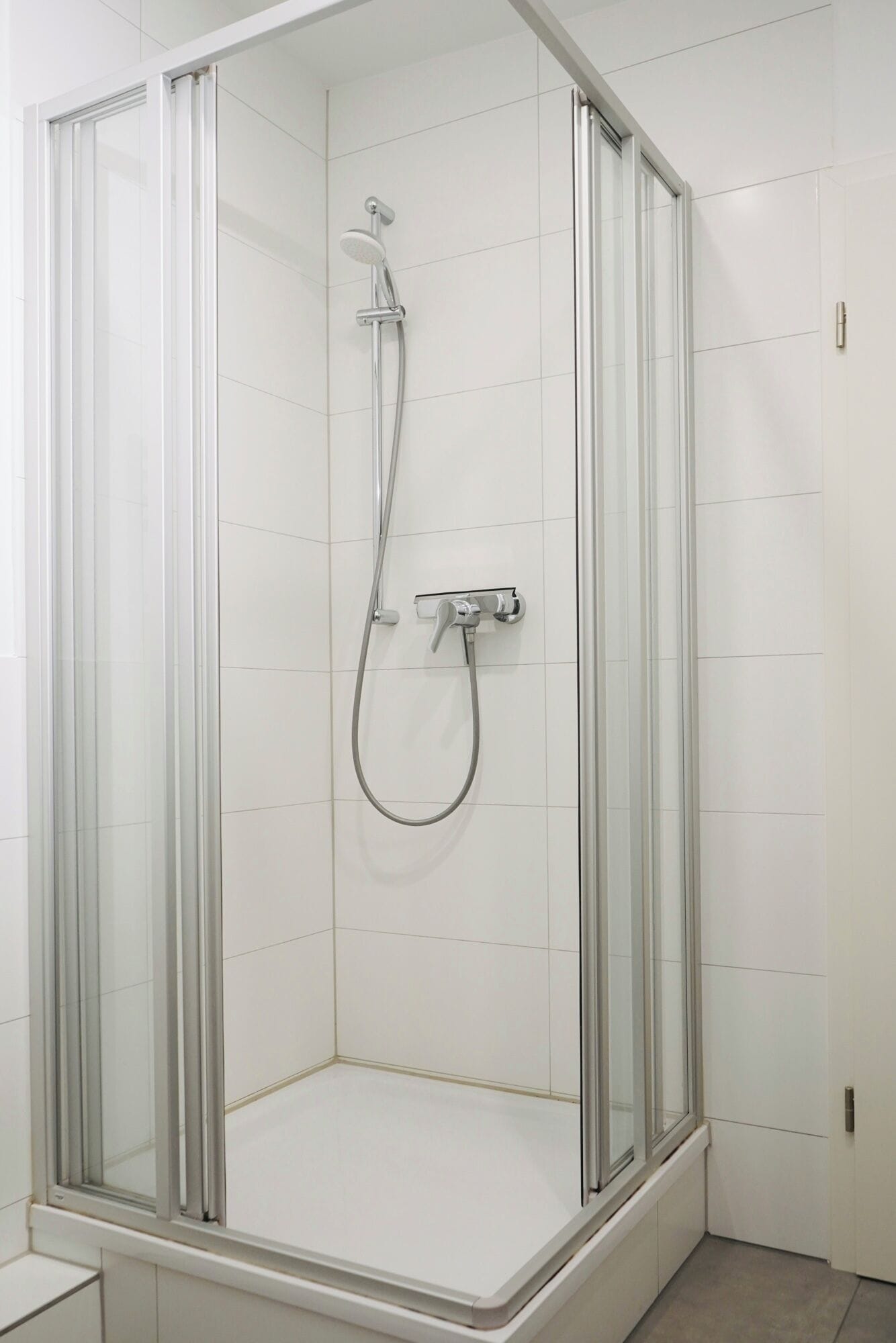 Un cubículo de ducha con paredes de vidrio, un cabezal de ducha manual y un grifo empotrado en la pared.