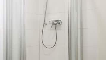 Un cubículo de ducha con paredes de vidrio, un cabezal de ducha manual y un grifo empotrado en la pared.