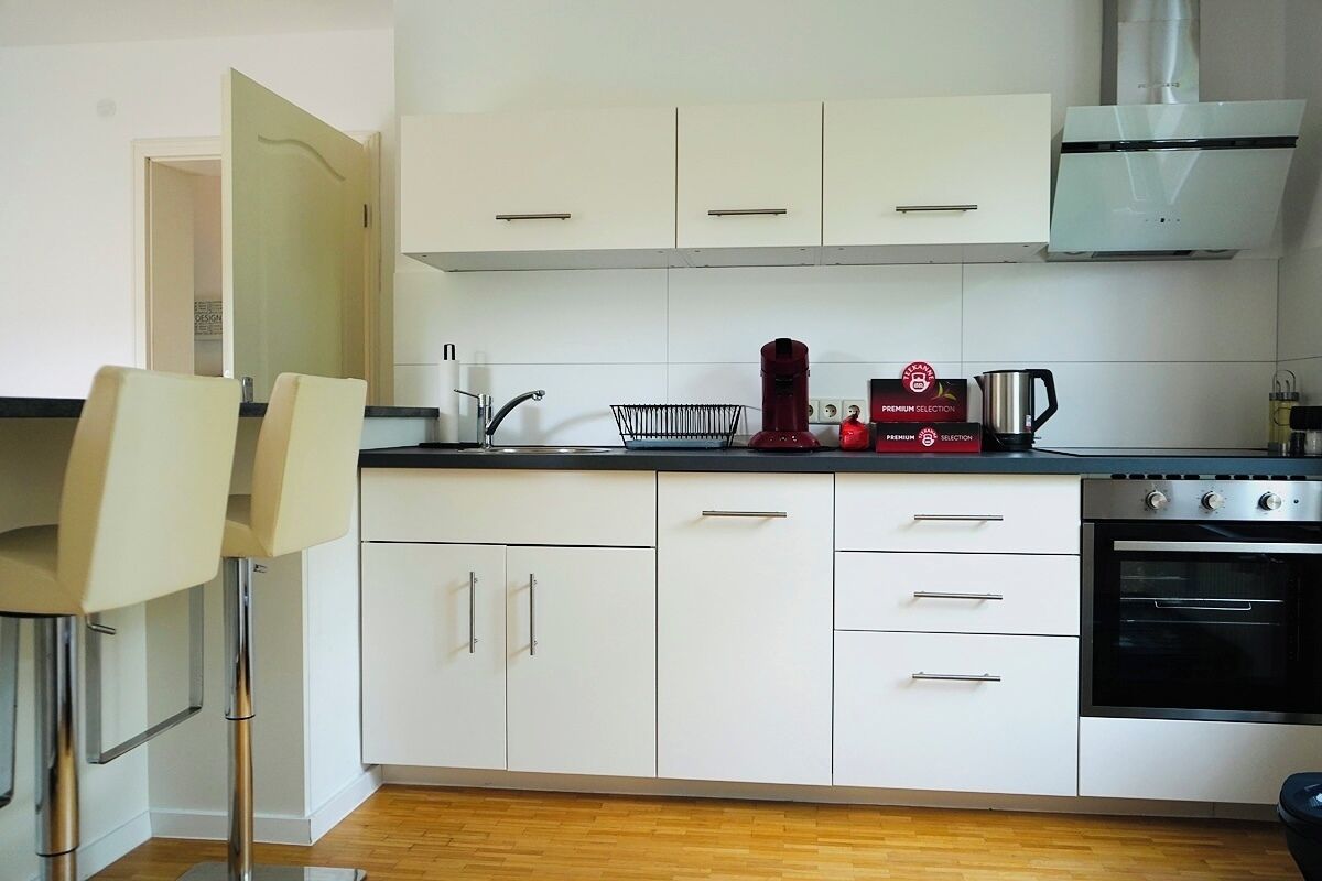 A modern kitchen with white cabinets, a stainless steel oven, and a coffee maker.