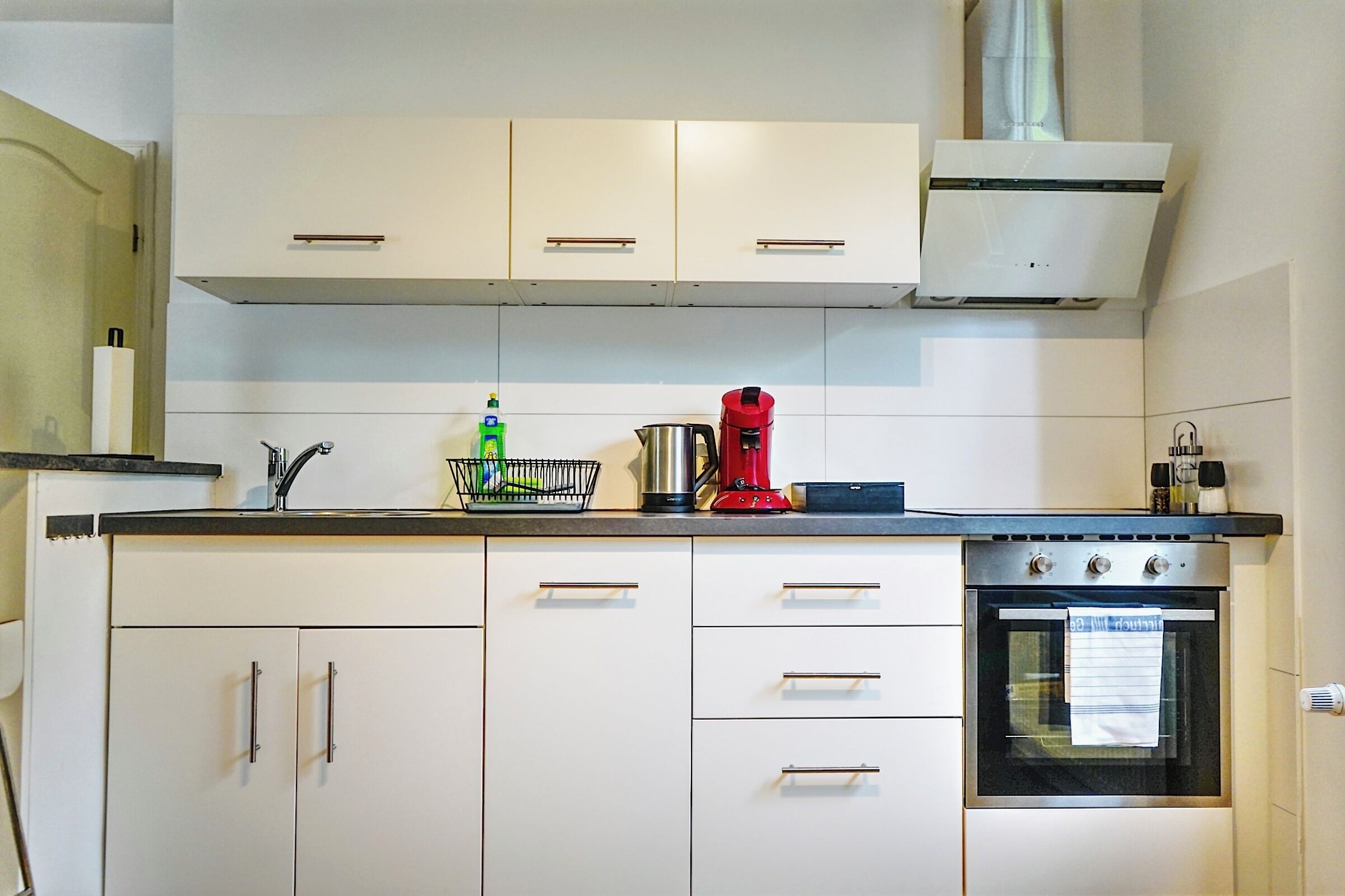 A kitchen with white cabinets, a stove, and a coffee maker.