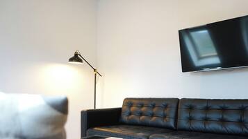Un salon avec un canapé en cuir noir, une table basse en verre, un lampadaire noir et un téléviseur à écran plat fixé au mur.