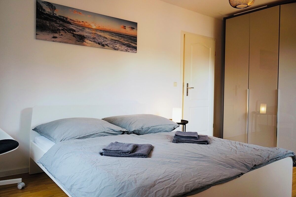 Un dormitorio con cama, almohadas, una mesita de noche, un armario y un cuadro en la pared.
