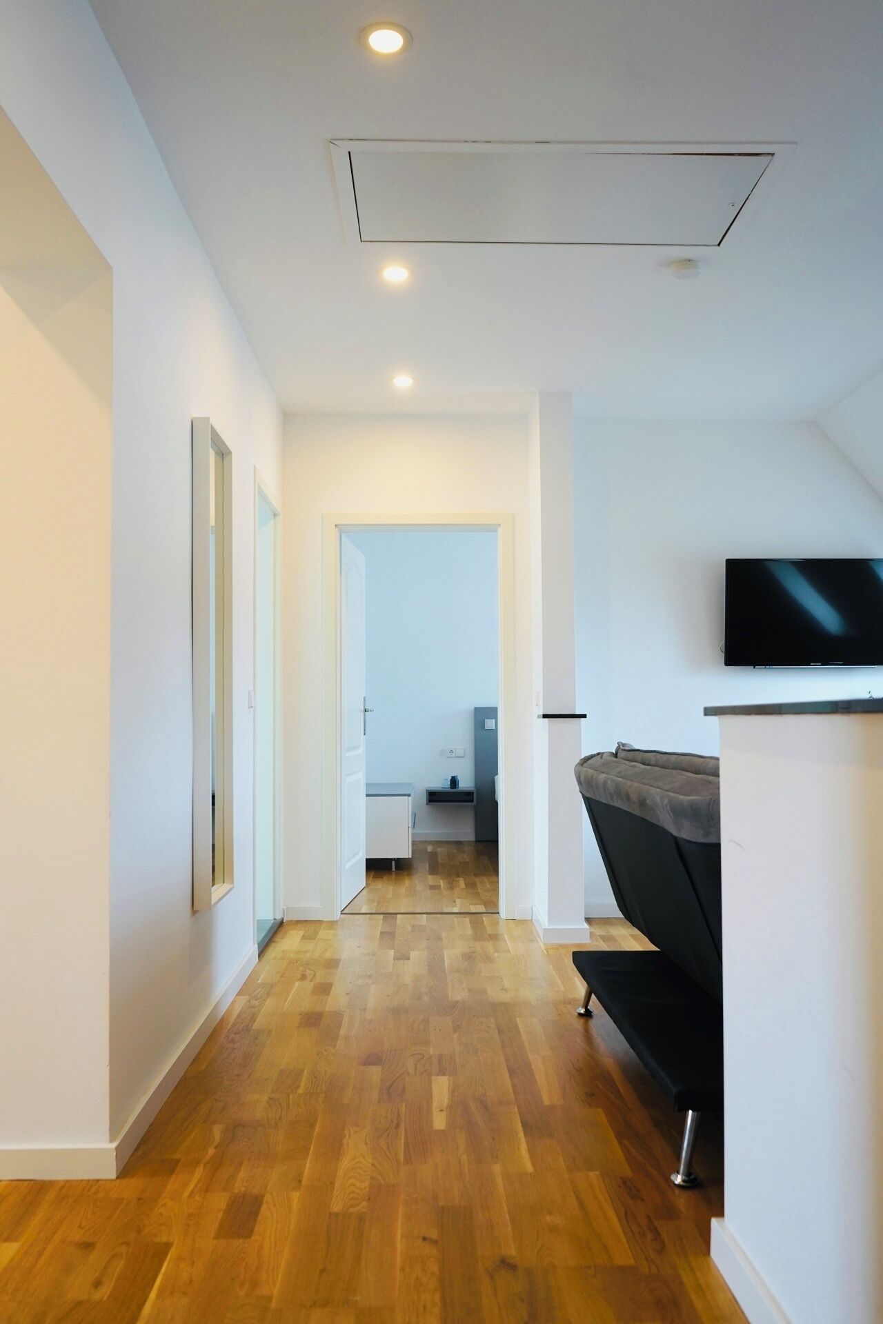Ein Flur mit Holzboden, einem an der Wand befestigten Flachbildfernseher und einer Couch in der Ecke.
