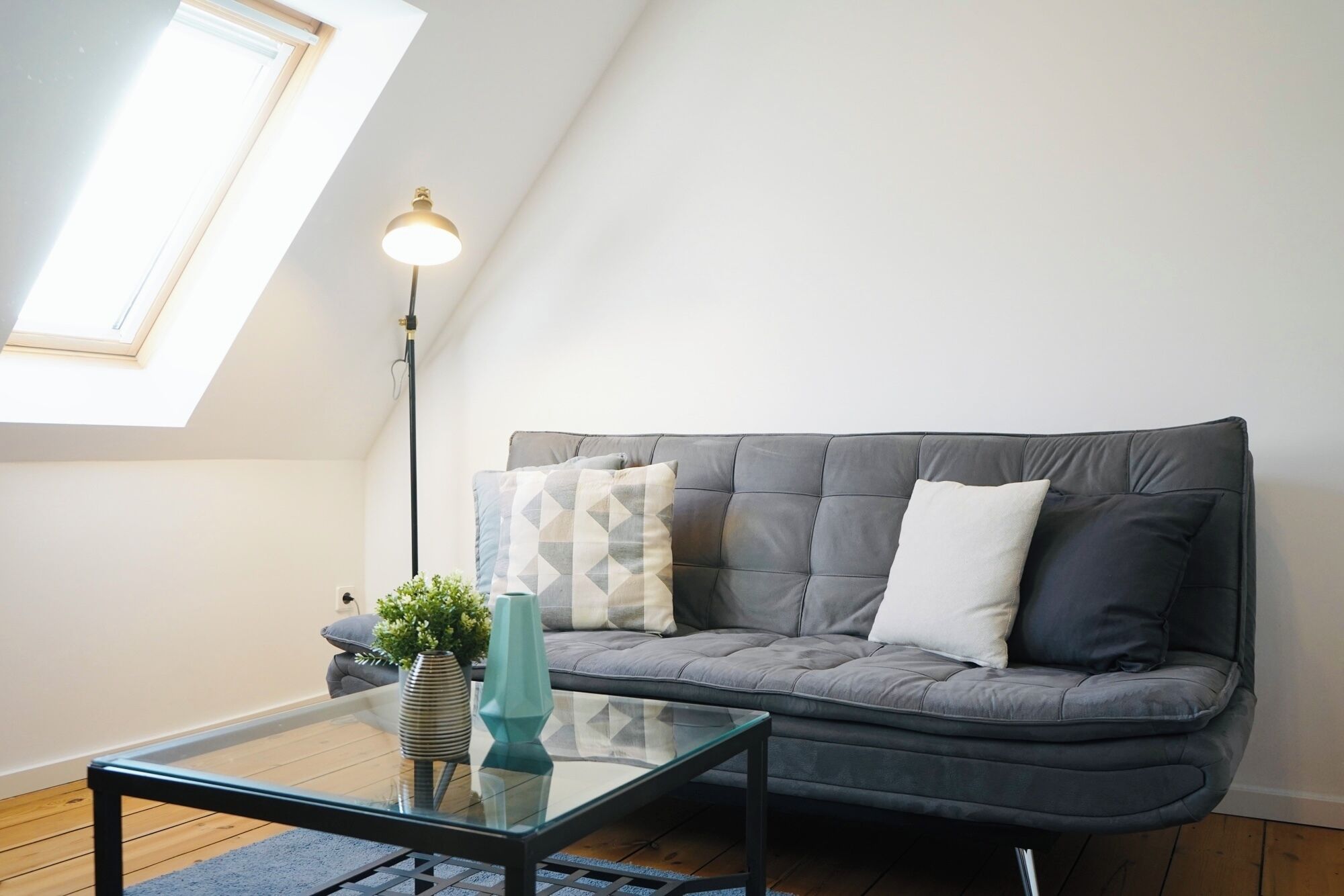 A modern living room with a grey sofa, a glass coffee table, and a floor lamp.