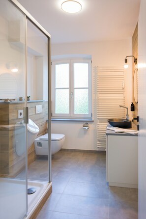 A modern bathroom with a glass shower enclosure, a toilet, a sink, and a window. - green-man Marktplatz Apartments (Wolfsburg)