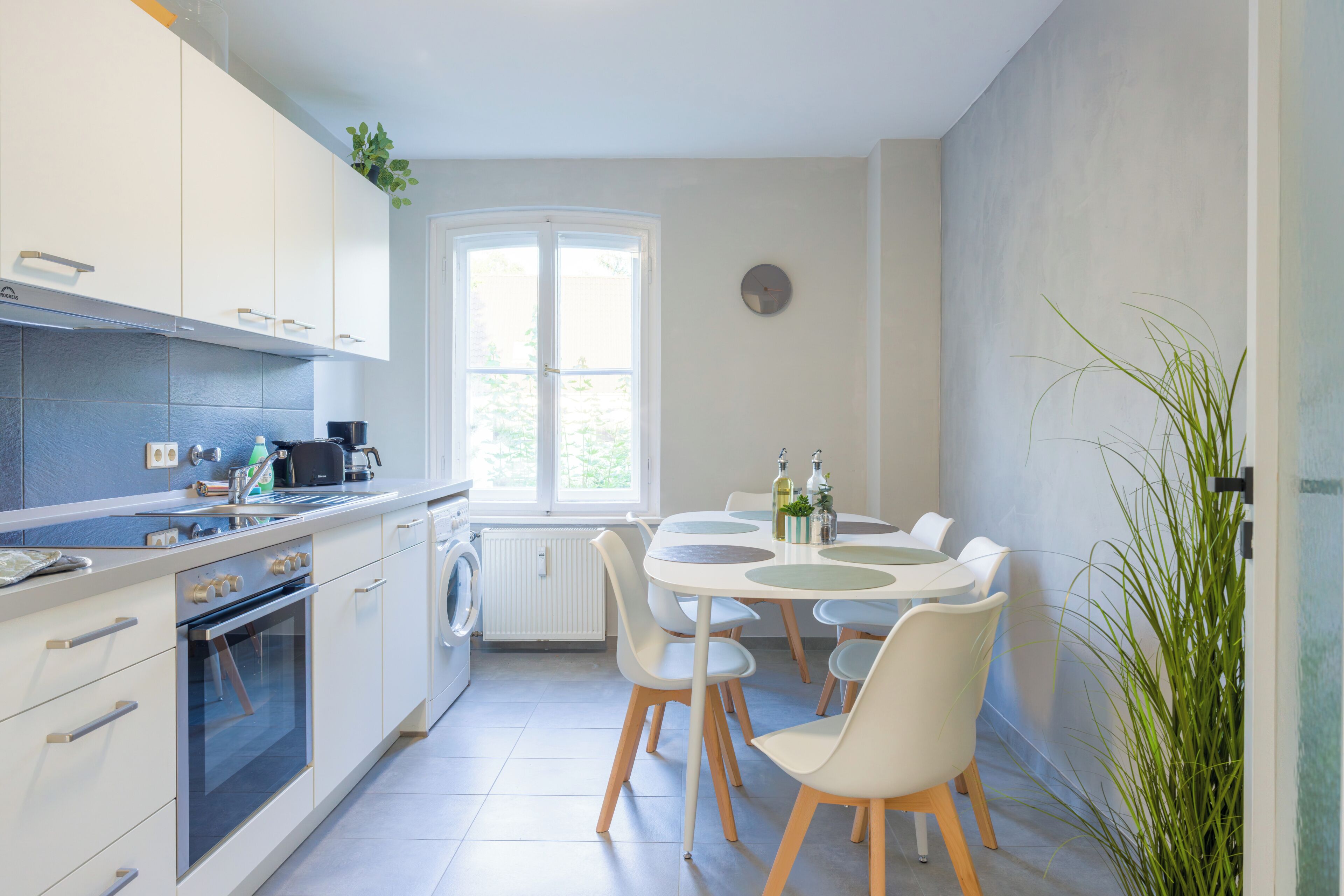 A modern kitchen with white cabinets, a built-in oven, and a dining area with a round table and chairs.