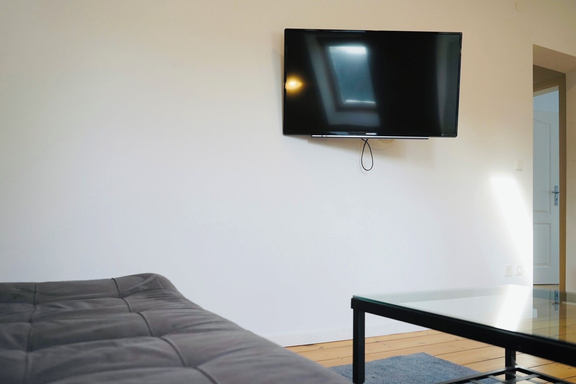 A room with a bed, a small table, and a mounted television on the wall.