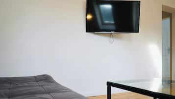 A room with a bed, a small table, and a mounted television on the wall.