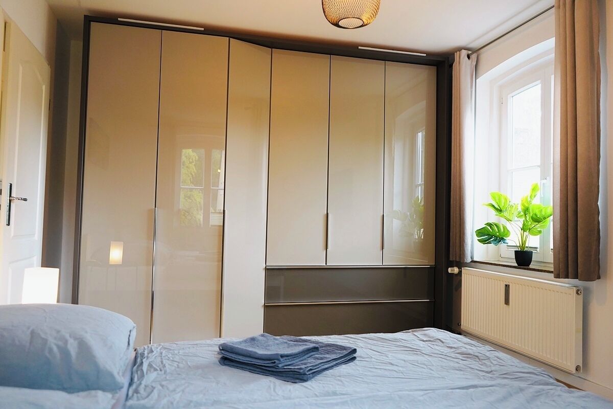 Een slaapkamer met een bed, een kast, een raam met gordijnen en een plant.