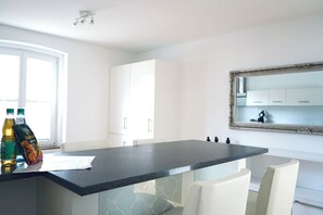 A modern kitchen with a central island, white cabinetry, and a large mirror above the countertop. - green-man Marktplatz Apartments (Wolfsburg)