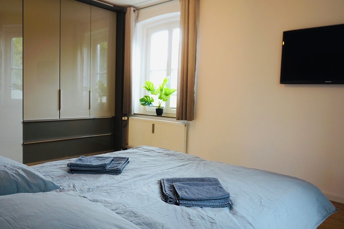 A bedroom with a bed, a wardrobe, a window with curtains, and a potted plant.