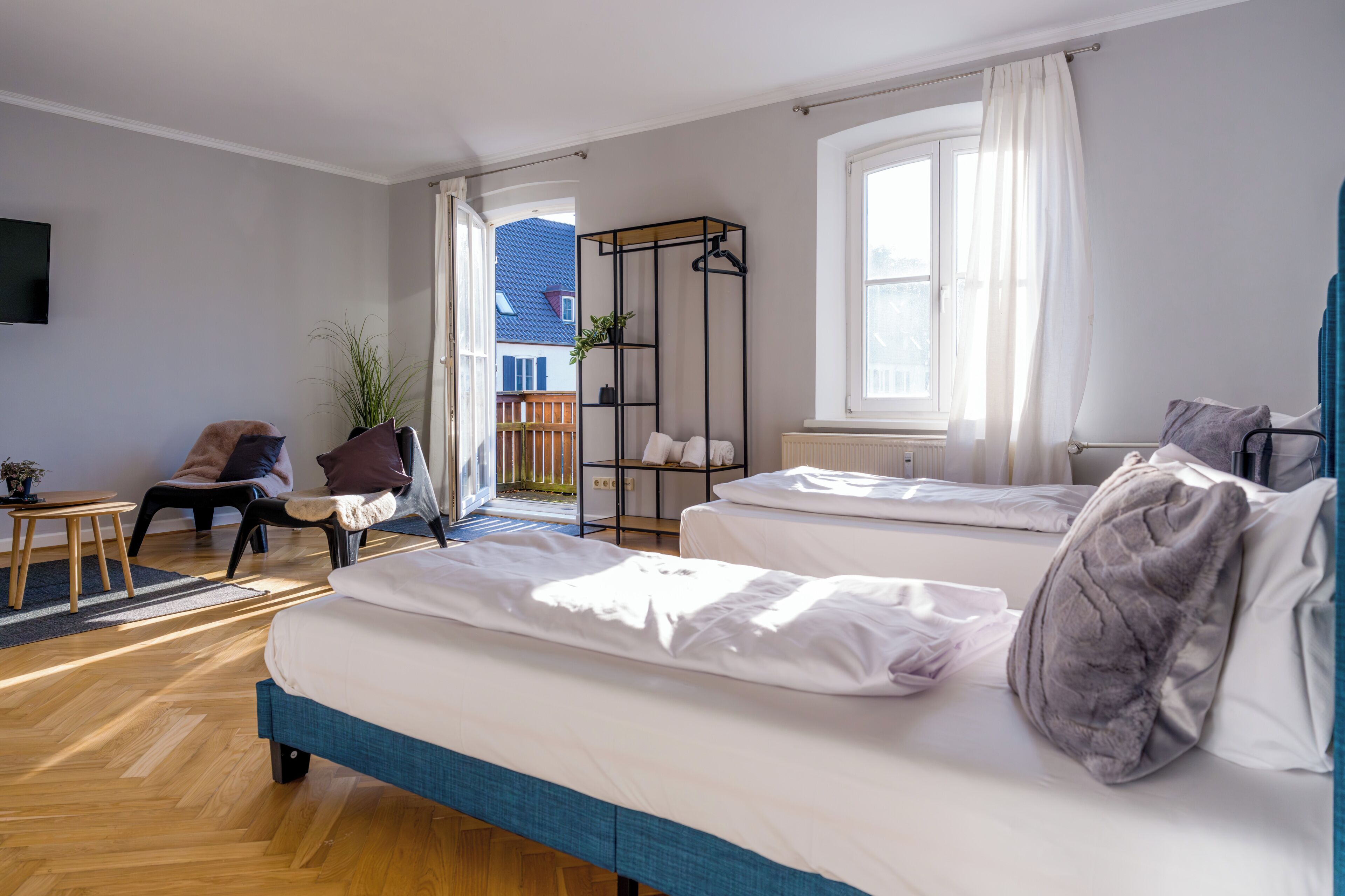 A bedroom with two beds, a chair, a small table, and a plant.