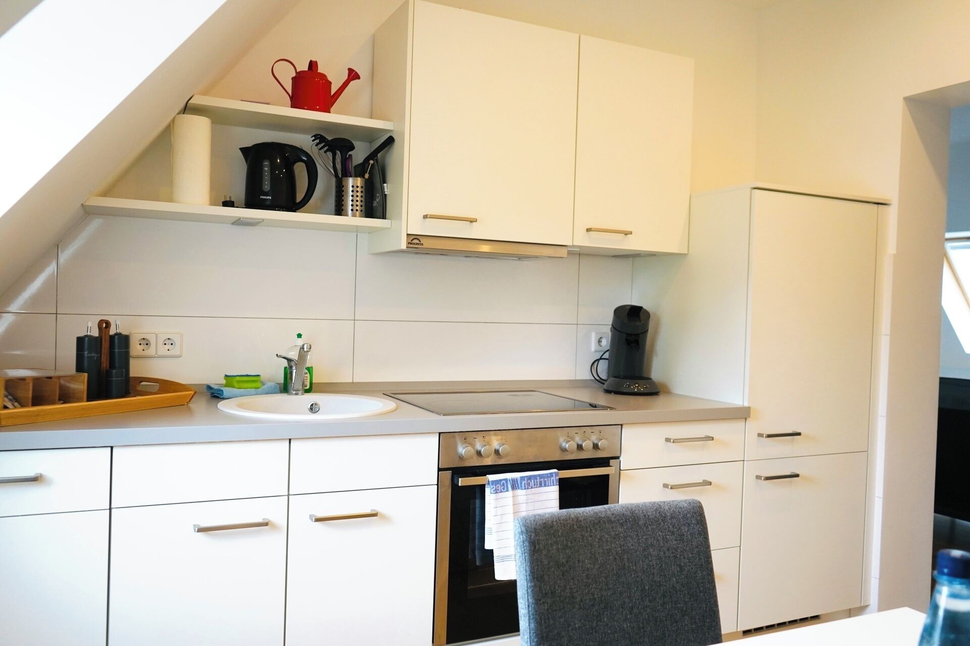 Eine moderne Küche mit weißen Schränken, einem Backofen, einem Wasserkocher und einer Kaffeemaschine.