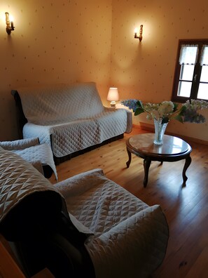 A room with a sofa, a round table with a vase of flowers, and a lamp.
