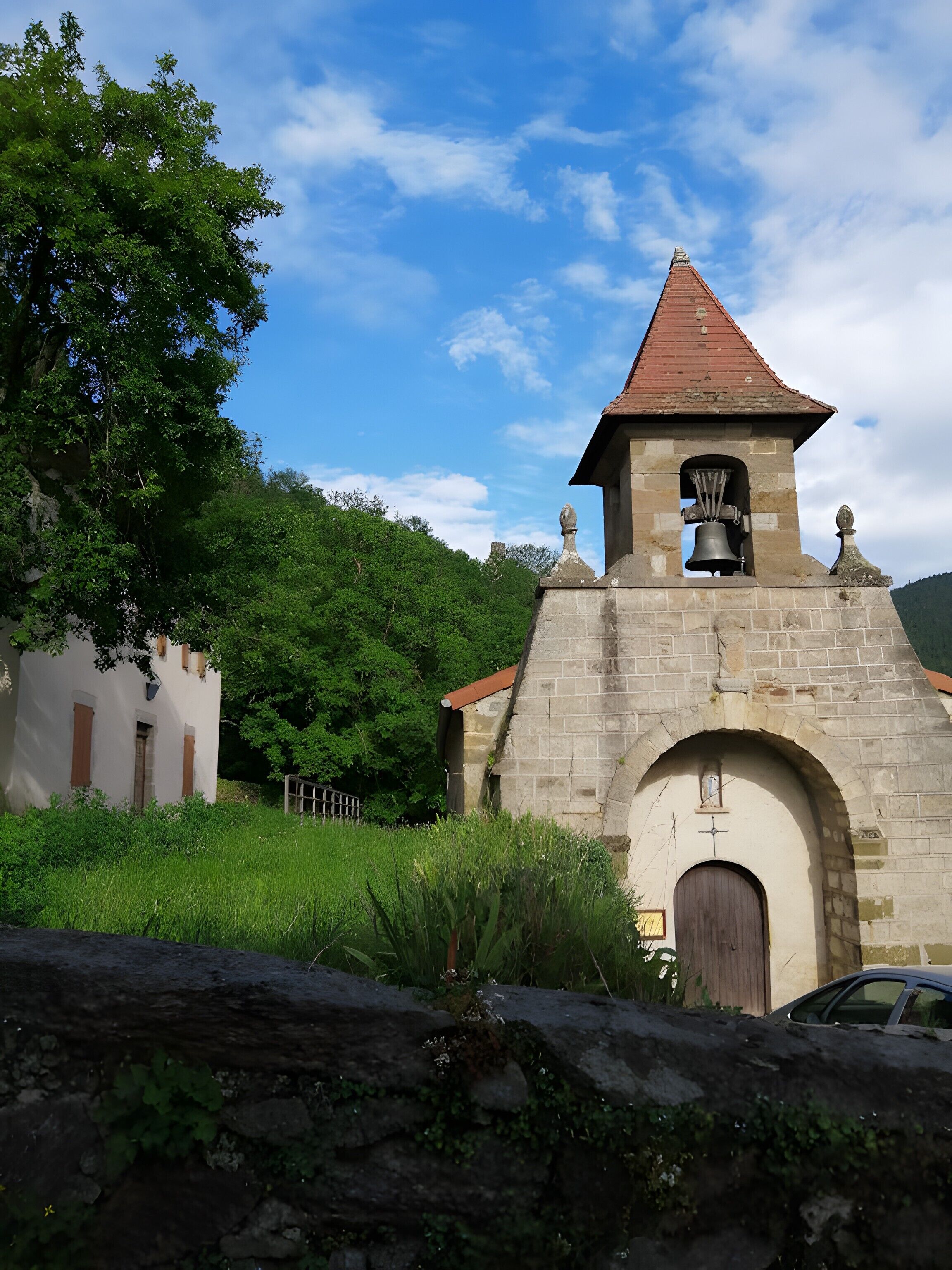 Un clocher en pierre surmonté d’un toit rouge, doté d’une entrée en arc de cercle et d’une cloche visible à travers la fenêtre.