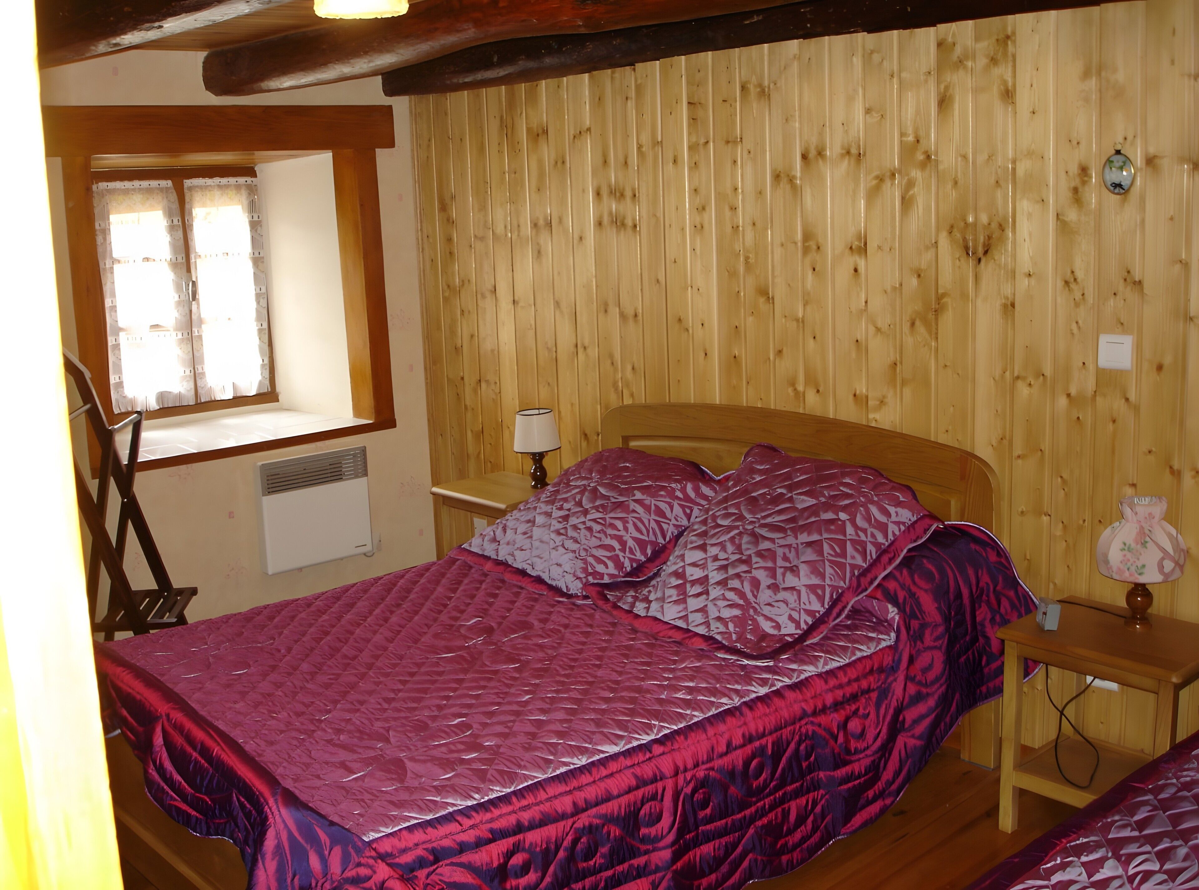 Een kamer met houten lambrisering, een bed, een raam, een lamp en een klein tafeltje.