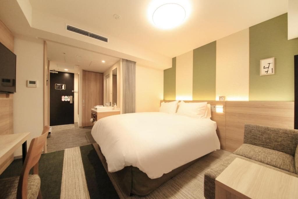 Ein Hotelzimmer mit einem großen Bett, einem Schreibtisch, einem Sessel, einer Couch und einem Fernseher.