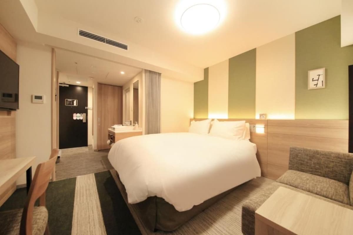 Quarto de hotel com uma cama grande, uma escrivaninha, uma cadeira, um sofá e uma televisão.