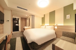 Quarto de hotel com uma cama grande, uma escrivaninha, uma cadeira, um sofá e uma televisão.