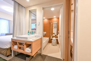 Een hotelkamer met een bed, een badkamer met een douche, een wastafel en een spiegel.