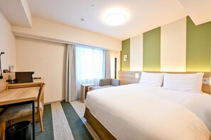 Quarto de hotel com uma cama, escrivaninha, cadeira e janela com cortinas.