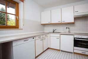 A kitchen with white cabinets, a dishwasher, a stove, and a window with a view of trees. - House at Gutach No. 12 (Titisee-Neustadt)
