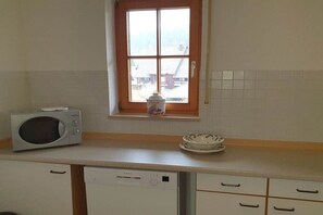 Une cuisine équipée d’un four à micro-ondes, d’un lave-vaisselle et d’une fenêtre donnant sur les bâtiments environnants.