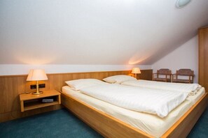 Un lit simple avec une tête de lit en bois, deux tables de chevet avec des lampes et une petite étagère avec une télécommande.