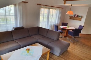 A living room with a sectional sofa, a dining table with chairs, and a lamp. - House at Gutach No. 12 (Titisee-Neustadt)