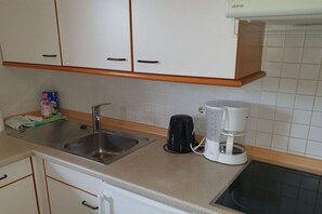 Une cuisine avec des meubles blancs, un évier en acier inoxydable, une machine à café noire et une cafetière blanche.