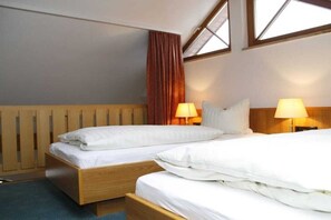 Ett hotellrum med två separata sängar, trägavlar, ett fönster med gardiner och sänglampor.