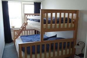 Une chambre avec deux lits superposés, une fenêtre avec des rideaux et une petite table avec une lampe.