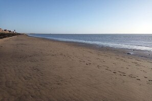 Une vaste plage de sable où l’on peut voir des empreintes de pas qui mènent jusqu’à l’eau.