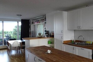 A modern kitchen with white cabinets, a wooden countertop, and a dining area with a table and chairs. - Holiday apartment with 1 bedroom (Wilhelmshaven)