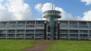Ein mehrstöckiges Gebäude mit einem zentralen Turm, großen Fenstern und einem Rasen im Vordergrund.