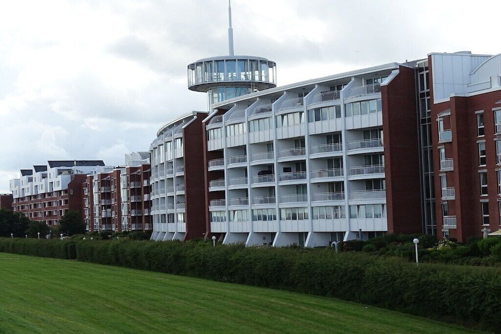 Ein modernes, mehrgeschossiges Wohngebäude mit Balkonen und einem zentralen Turm.