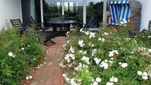 Eine Terrasse im Freien mit Tisch und Stühlen, umgeben von weißen Blumen und einem Pflasterweg.
